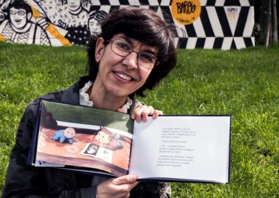 Almudena Ortega mostrando sonriente las páginas interiores del cuento Yo Quiero Tocar la Luna, del que es autora